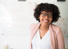 Smiling businesswoman with glasses and afro hairstyle in an office setting.